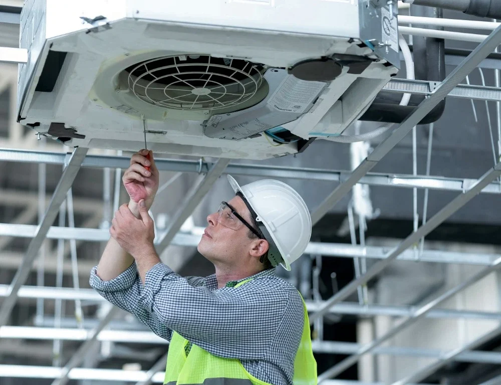 An engineer in a hi-vis jacket opening an air conditioning unit.