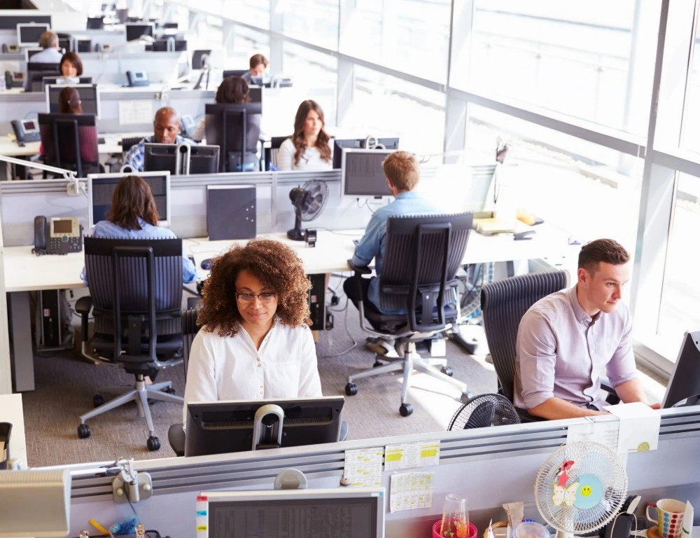 A busy open-plan office with lines of white desks.