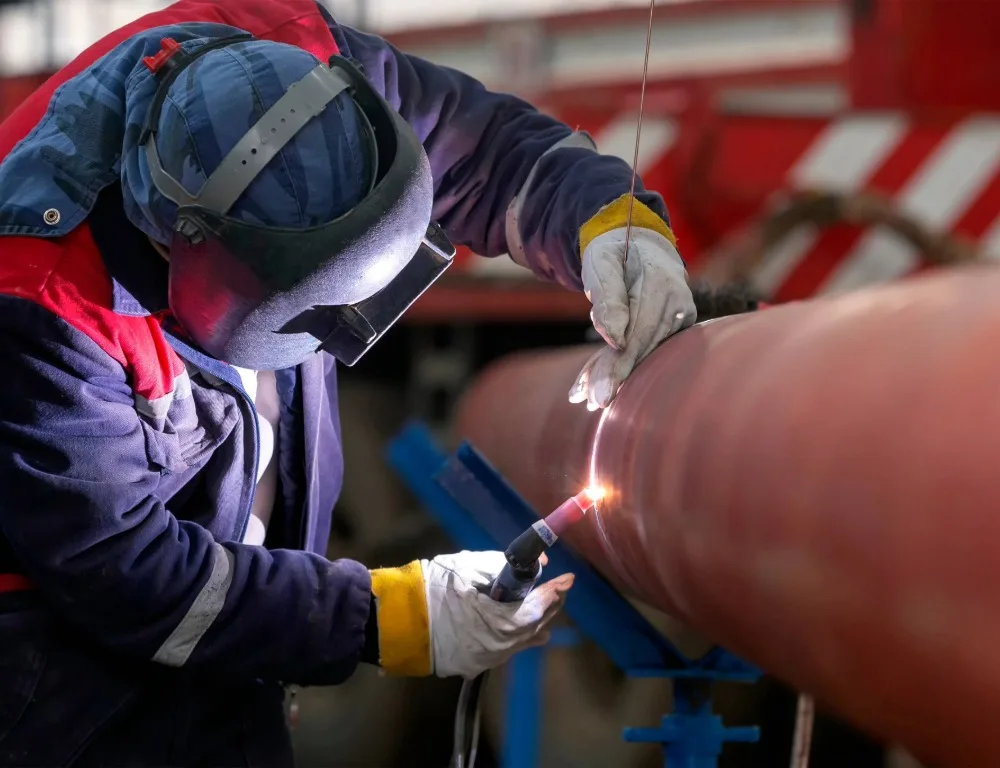 A welder fitting a new section of industrial pipe.