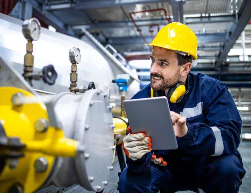 An engineer carrying a clipboard checks a gas pipe.