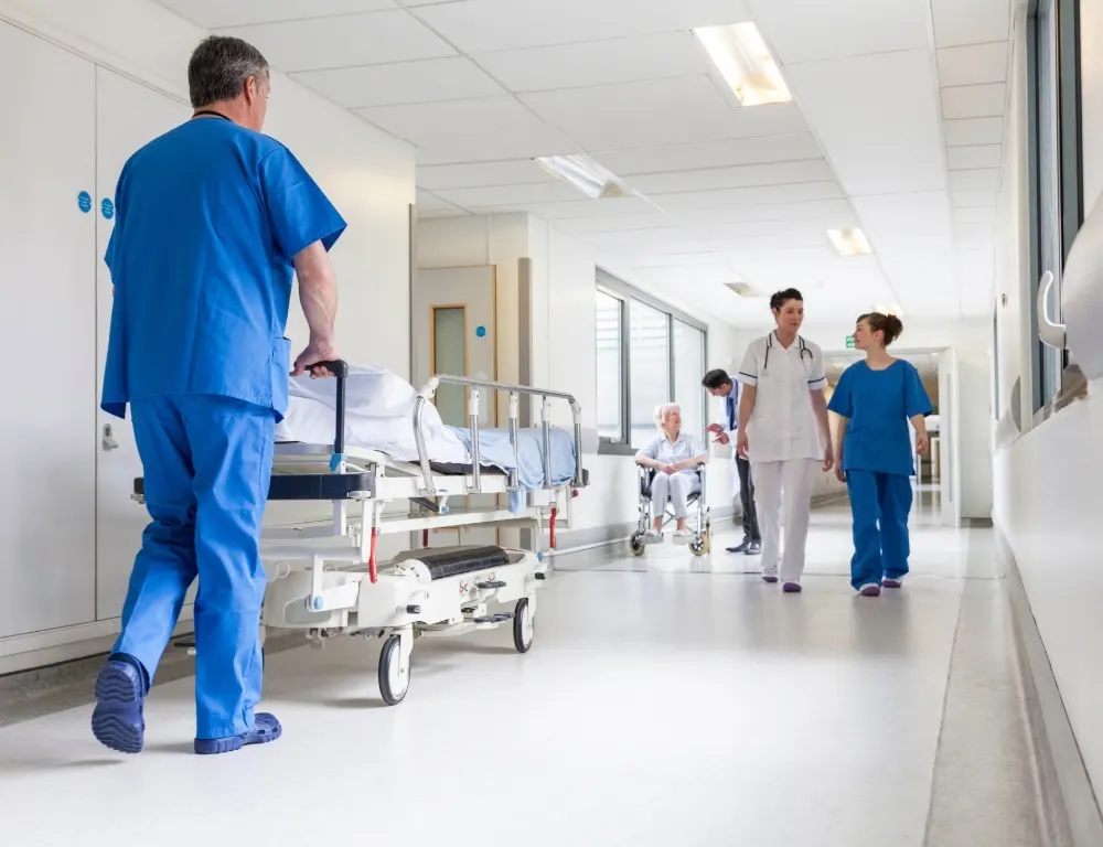A healthcare worker pushing a bed down a hospital corridor.