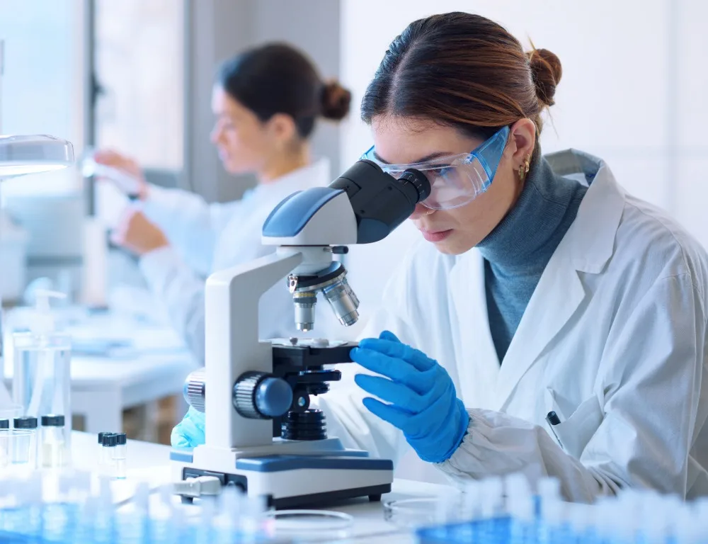 A woman wearing a lab coat uses a microscope.